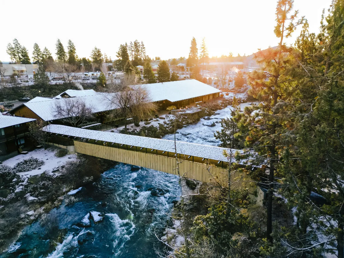 This peaceful exterior scene features a covered bridge over a flowing river, surrounded by trees and distant mountains. The natural setting is ideal for pet walks, trail exploration, and outdoor activities, with evident access to nearby hiking trails and green spaces that guests and their pets can enjoy.