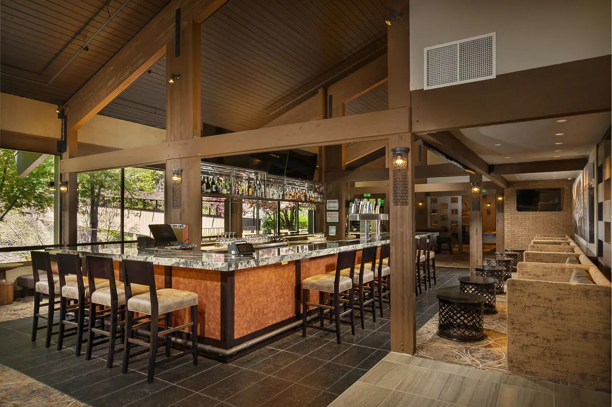 This interior image showcases a stylish bar area with a welcoming seating space, bottles attractively displayed on shelves, and a relaxed vibe conducive to socializing and unwinding. The space is warm and inviting, reflecting the atmosphere couples might enjoy during a romantic dinner or an evening drink at the lodge.